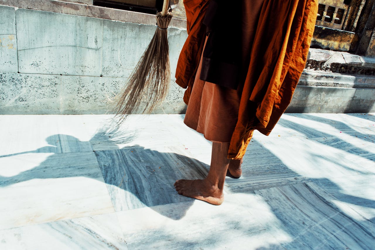 A Buddhist monk sweeping the marble courtyard in Bodhgaya, India. Captured in sunlight, highlighting spiritual simplicity.